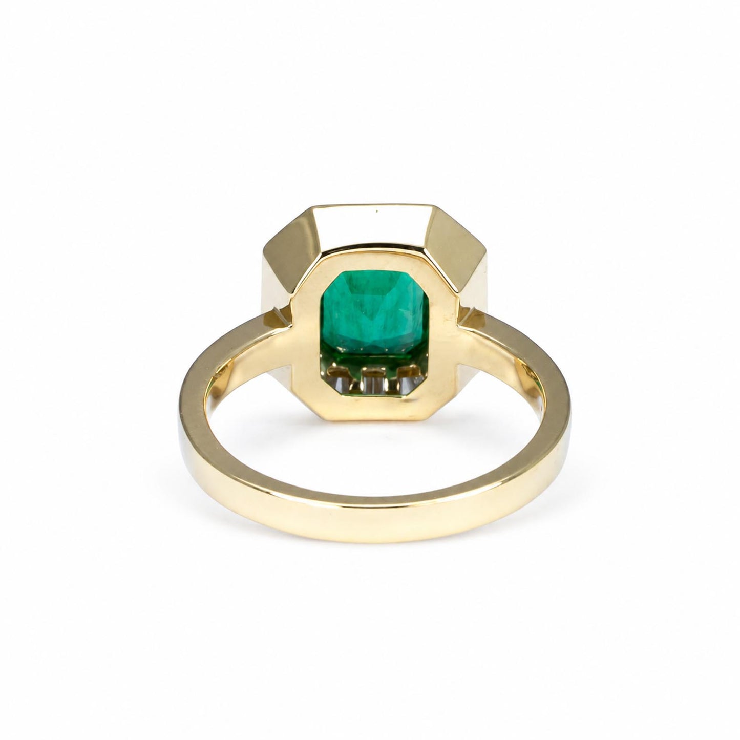 Back view of a  gold ring featuring a  faceted emerald-cut emerald, shown on a clean white background.