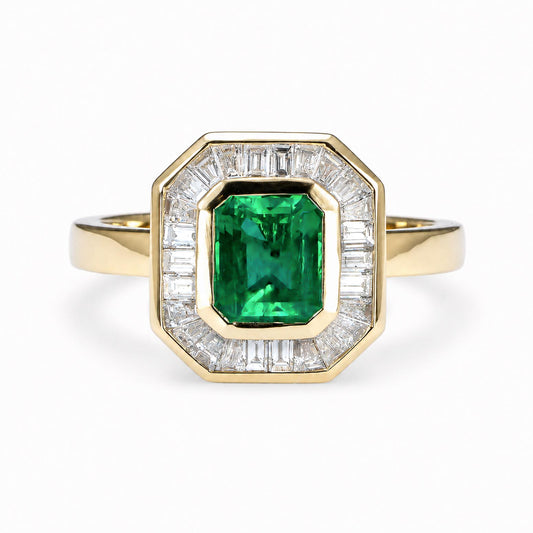 A yellow gold ring featuring an emerald-cut natural Colombian emerald in the center, surrounded by a halo of baguette-cut diamonds, set against a plain white background.