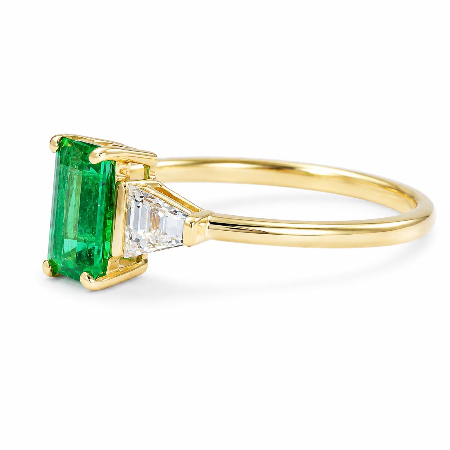 side view of a yellow gold ring featuring a rectangular emerald-cut emerald and a baguette-cut diamond, shown on a clean white background.