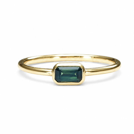 Yellow gold ring holding an Australian teal sapphire in emerald cut shape that is bezel set, shown on a white background