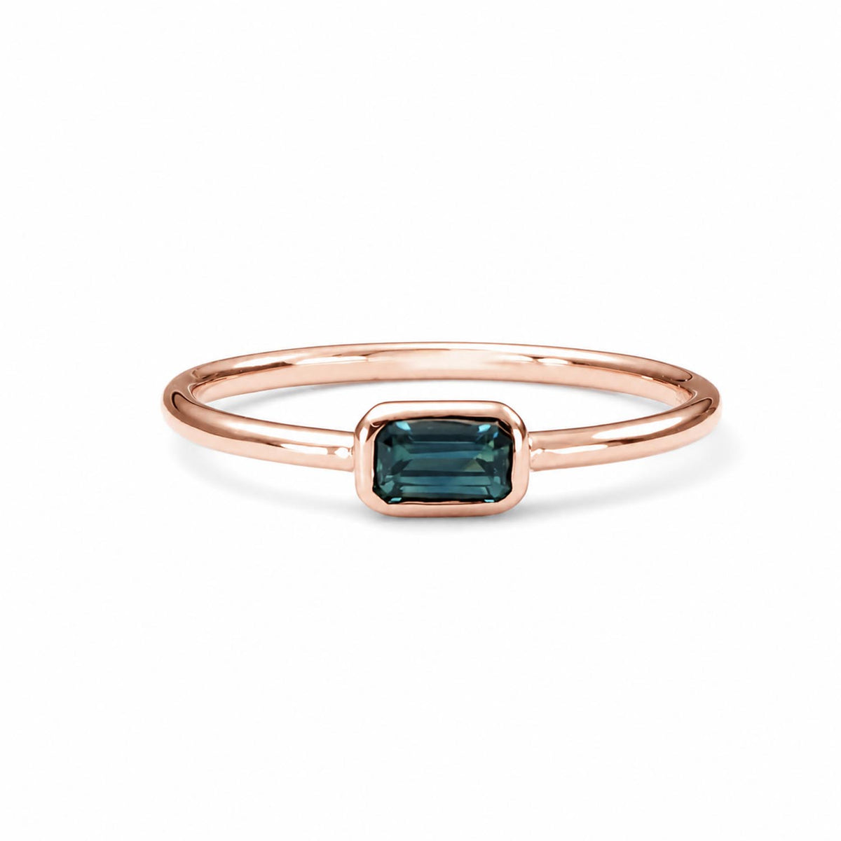 rose gold ring holding an Australian teal sapphire in emerald cut shape that is bezel set, shown on a white background