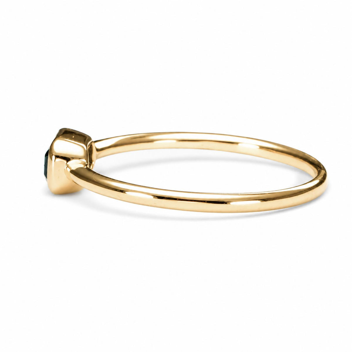side view of a Yellow gold ring holding an Australian teal sapphire in emerald cut shape that is bezel set, shown on a white background
