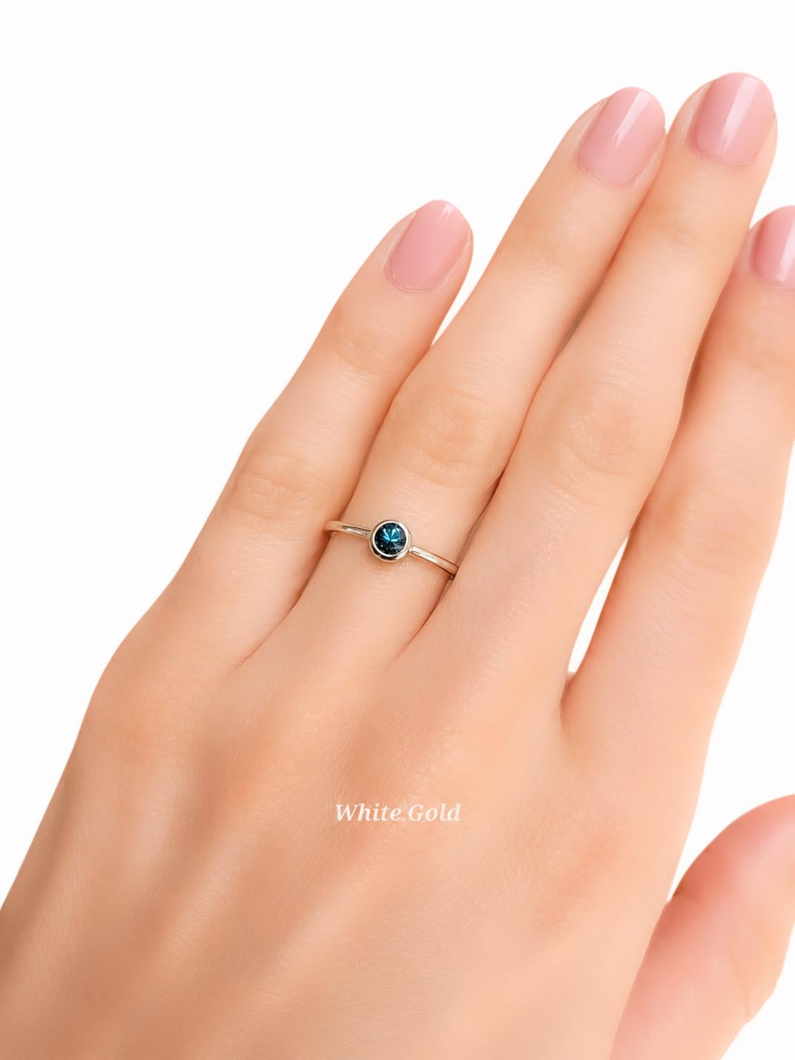 A close-up of a hand wearing a delicate white gold ring with a small Australian sapphire, set against a plain white background with a 'WhiteGold' text overlay.