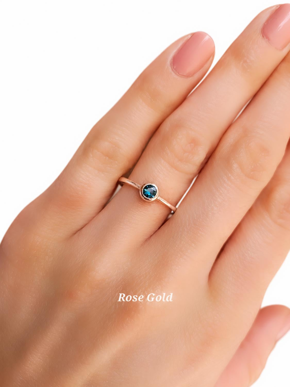 A close-up of a hand wearing a delicate rose gold ring with a small Australian sapphire, set against a plain white background with a 'Rose Gold' text overlay.
