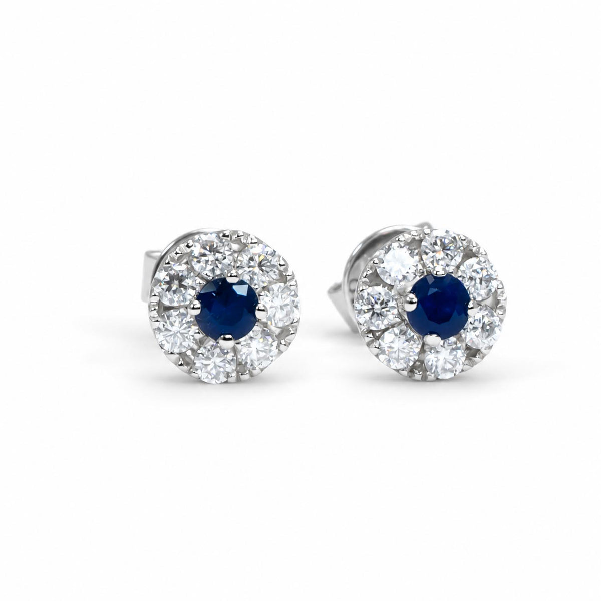Pair of 9K white gold earrings with a centre blue sapphire on a white background