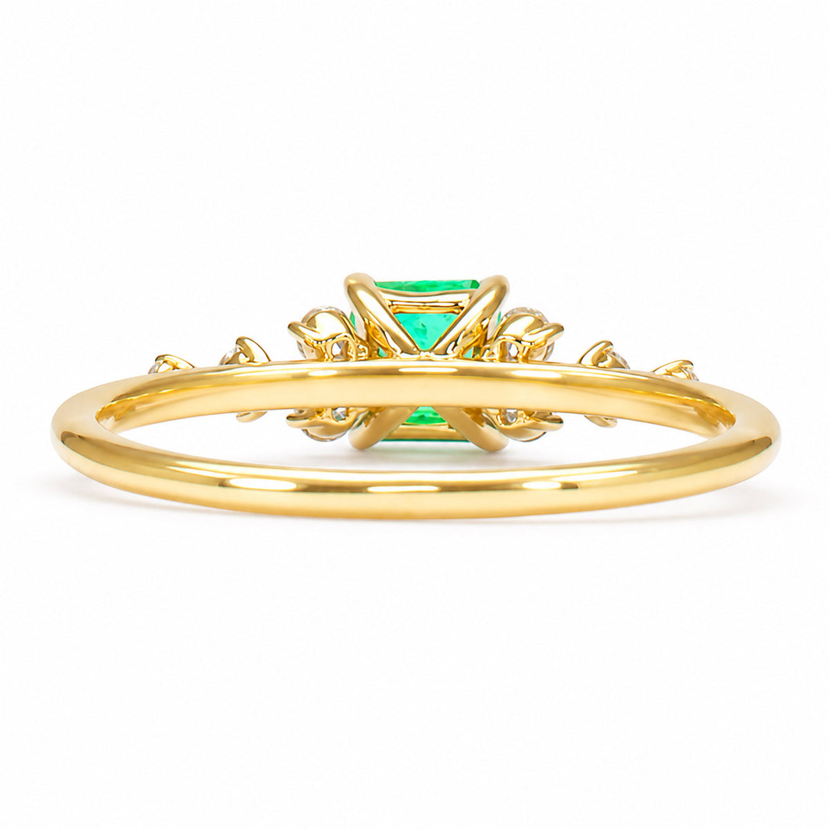 A gold ring with a central emerald gemstone and intricate gold details, shown from the back on a white background.