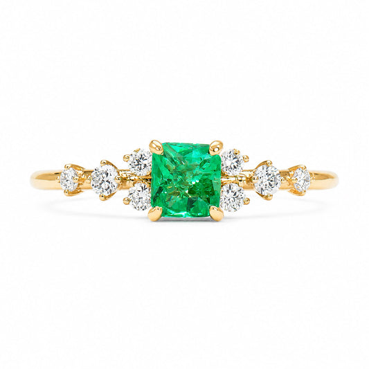 A gold ring with a square cut Colombian emerald in the centre and accent round diamonds on the shank on a white background