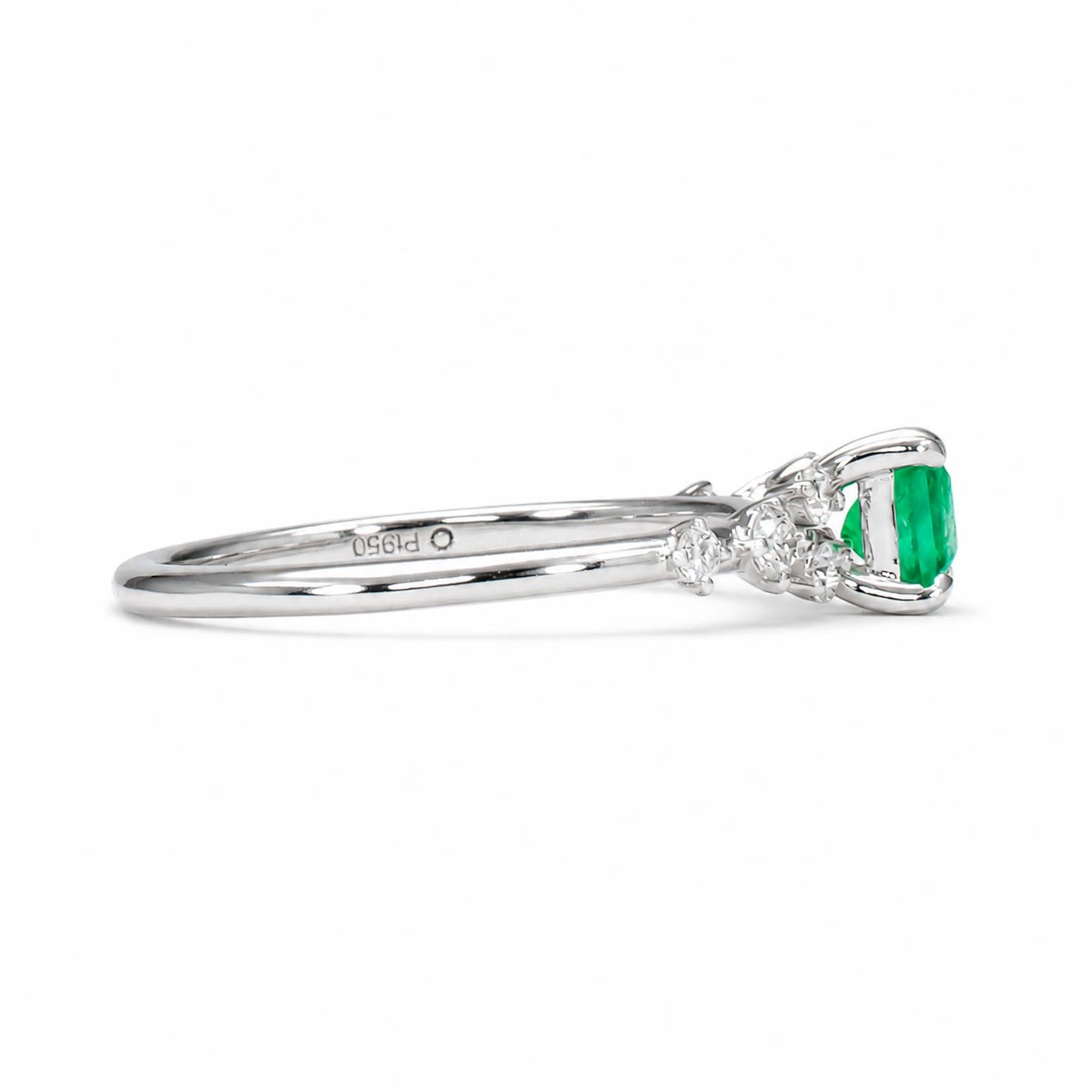 A platinum emerald and diamond ring featuring an emerald cut Colombian emerald center stone and small round diamonds on the shoulders, shown in profile against a white background.