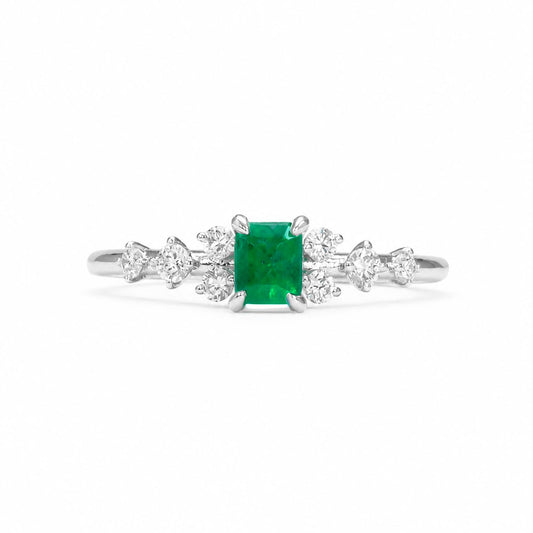 A platinum ring featuring an emerald-cut Colombian emerald center stone and round-cut diamonds on each side, set against a plain white background.