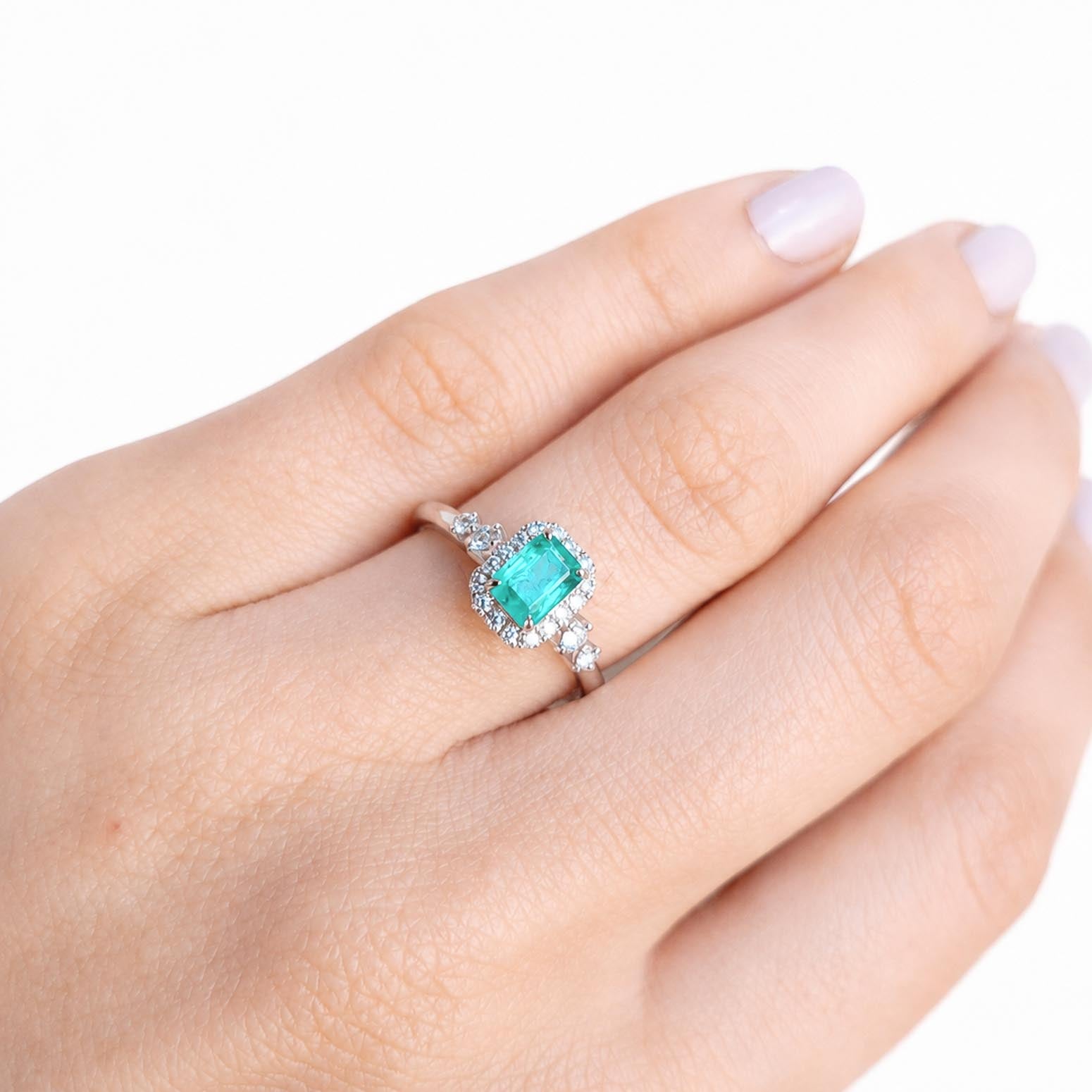 A close-up of a hand wearing a platinum ring with an emerald-cut Colombian emerald center stone and diamond accent stones.