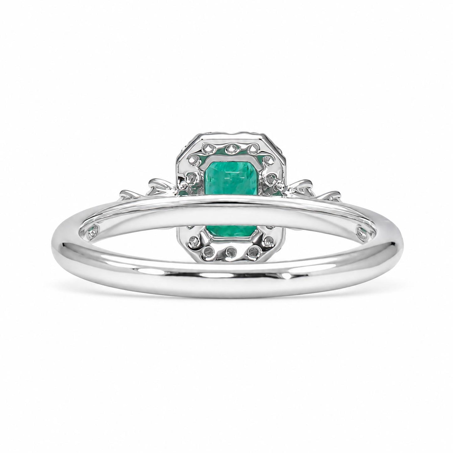 Back view of a platinum ring featuring a central emerald-cut emerald surrounded by diamonds, set on a polished platinum band with decorative  details.