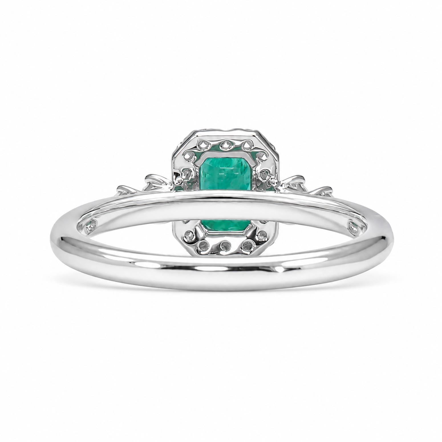 Back view of a platinum ring featuring a central emerald-cut emerald surrounded by diamonds, set on a polished platinum band with decorative  details.