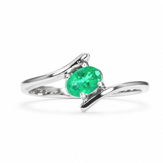A white gold ring featuring an oval-cut Colombian emerald in a prong setting, with a split shank band design, shown on a clean white background.