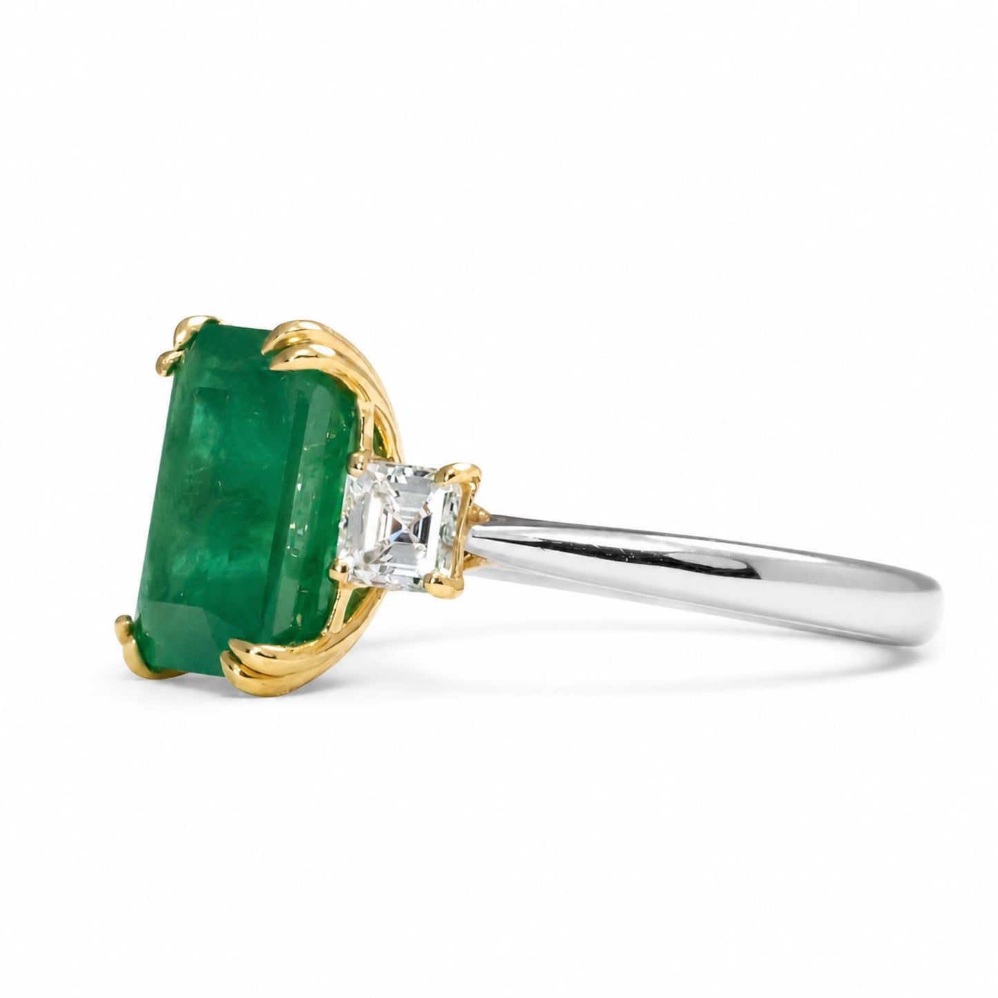 A ring featuring a rectangular emerald-cut Colombian emerald in a yellow gold setting, with square diamonds on a polished platinum band, shown on a white background.