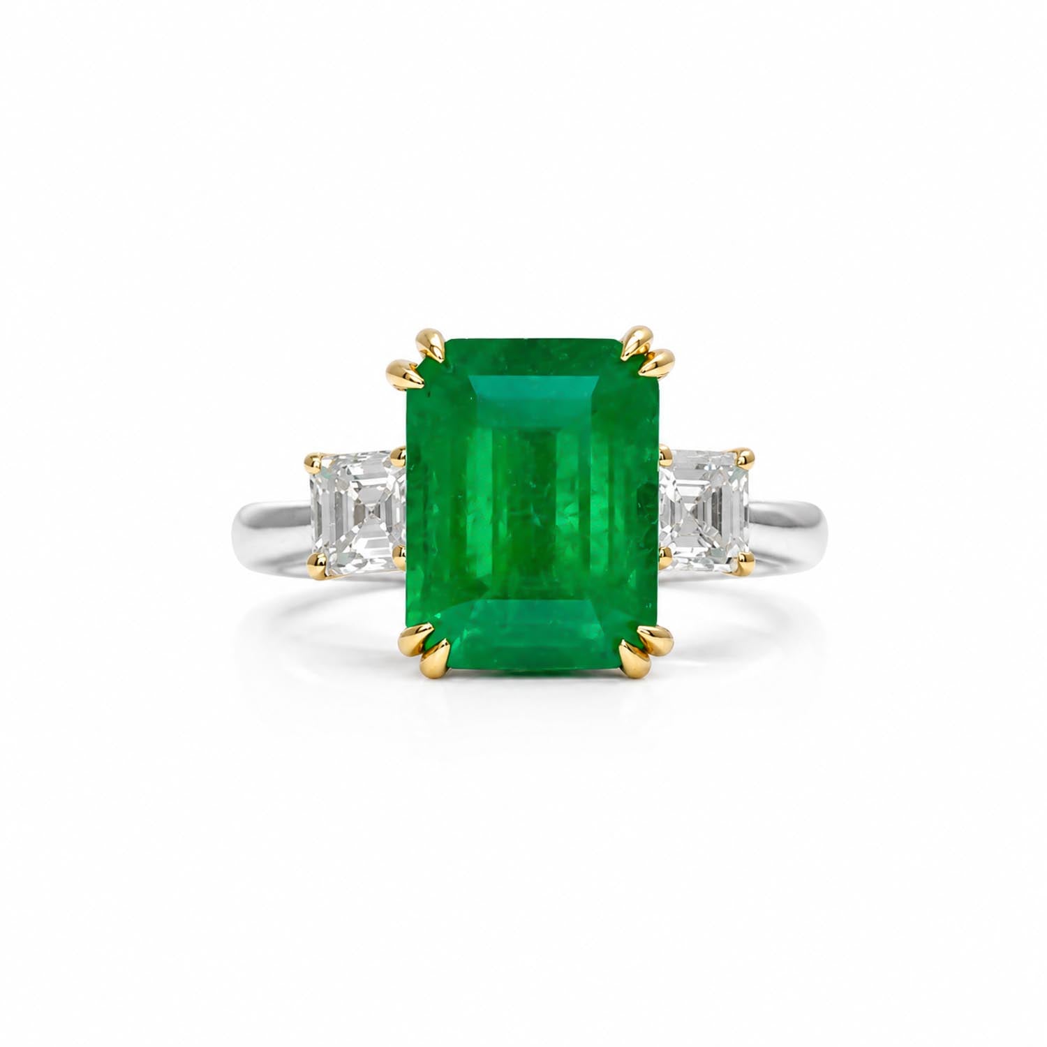 An emerald-cut Colombian emerald ring with set in double prong yellow gold and emerald-cut diamonds on a platinum band, set against a plain white background.