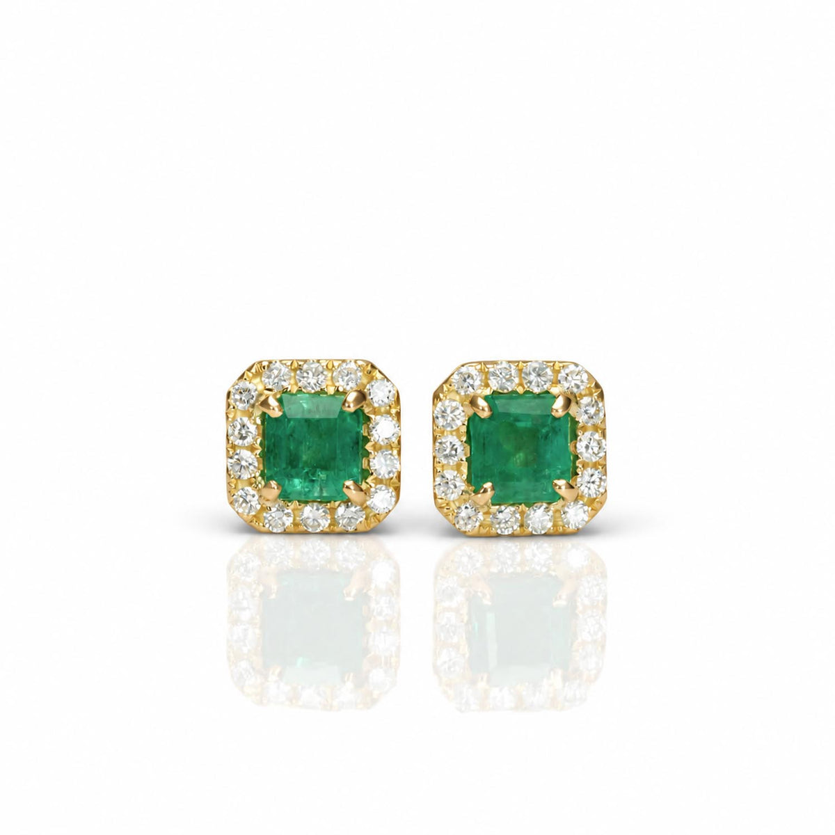 A pair of 18K yellow gold square stud earrings featuring a central Colombian emerald. emerald-cut gemstone, surrounded by a halo of diamonds, shown on a white background with a soft reflection below.