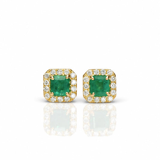 A pair of 18K yellow gold square stud earrings featuring a central Colombian emerald. emerald-cut gemstone, surrounded by a halo of diamonds, shown on a white background with a soft reflection below.