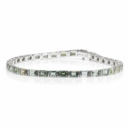 a platinum tennis bracelet featuring teal sapphires shown on a white background