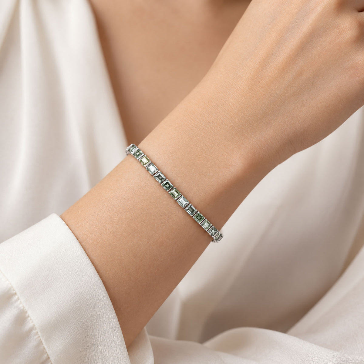 a platinum tennis bracelet with princess cut teal sapphires shown being worn on a wrist