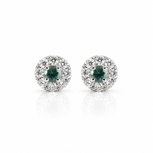 a pair of platinum earrings featuring alexandrite centres and a halo of diamonds, shown on a white background with a soft reflection
