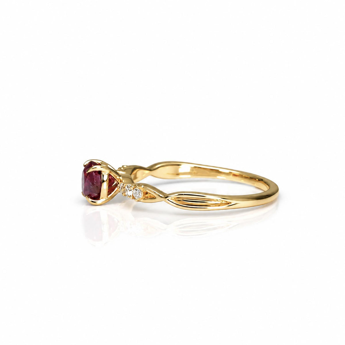 A yellow gold ring featuring an oval-cut ruby in a prong setting, accented by  small diamonds on the band, shown on a white background with a soft reflection.