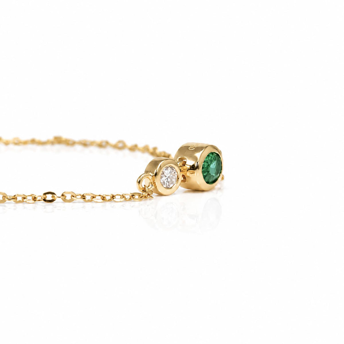 A gold chain bracelet featuring a oval gold setting with an oval green emerald and a smaller bezel-set round diamond.