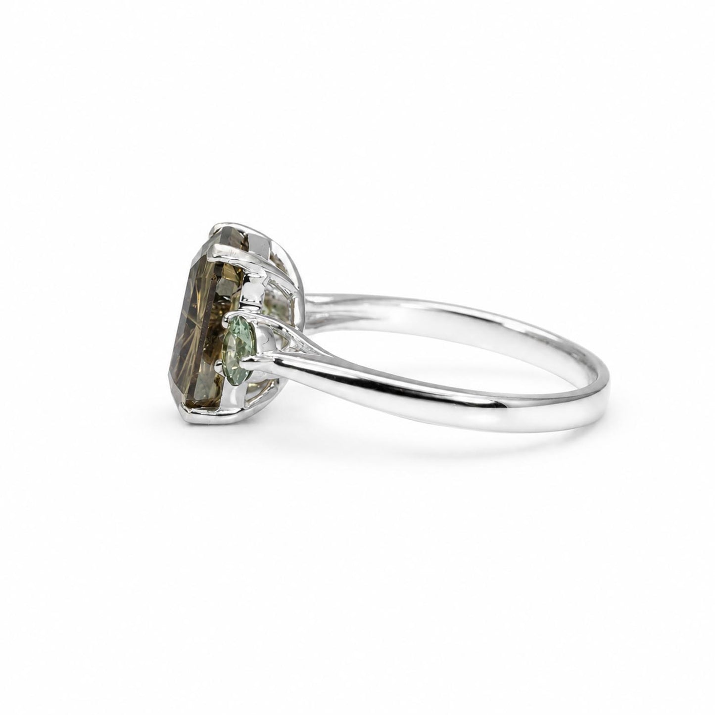 A white gold ring featuring a large, rectangular, ocatagon-cut green brown sapphire with teal green round Australian sapphire accent stones, set in a polished band against a white background.