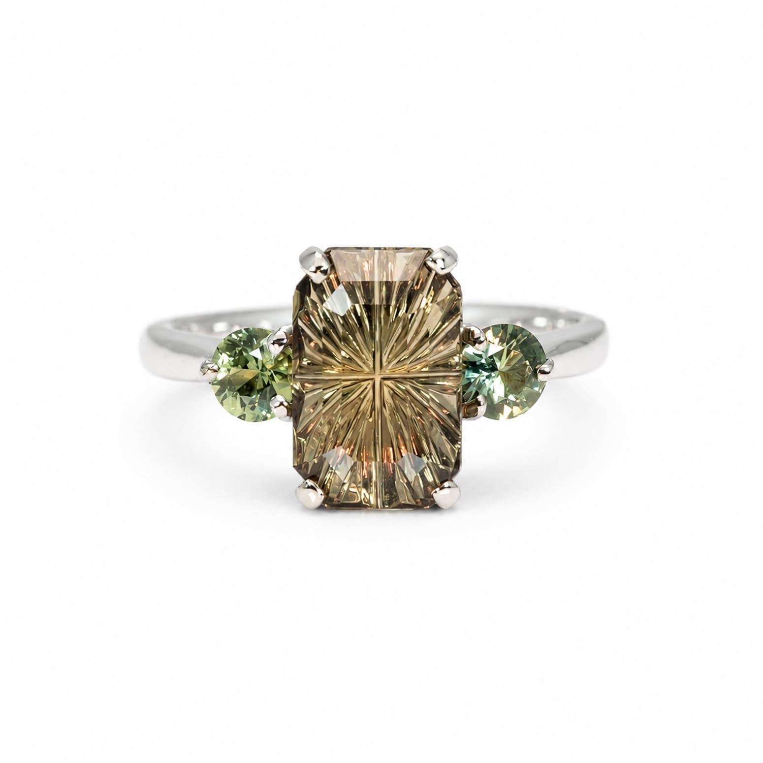 A white gold three-stone ring featuring a large rectangular octagon-cut brown gemstone in the center, flanked by two round teal green Australia sapphires on a white background.