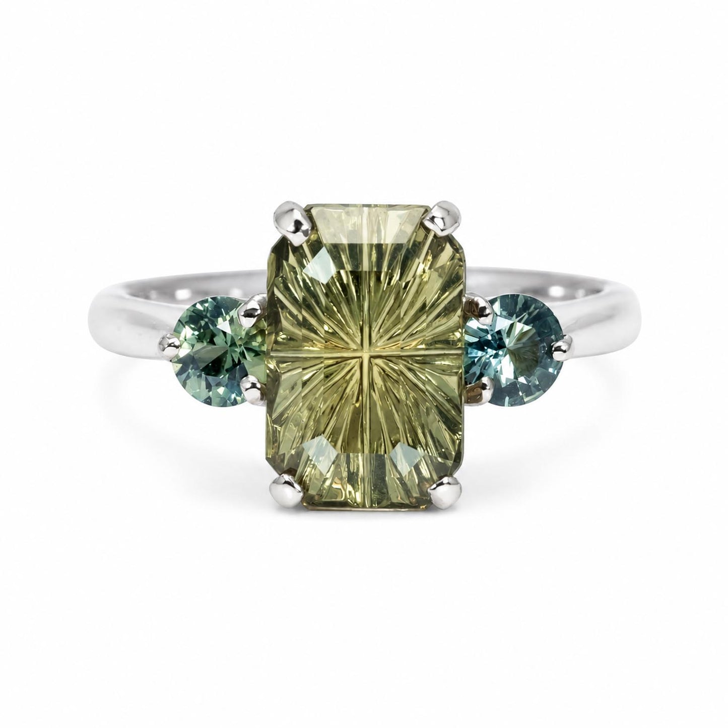A white gold three-stone ring featuring a large rectangular cut olive green sapphire with two round-cut teal blue Australian sapphires, set on a plain white background.