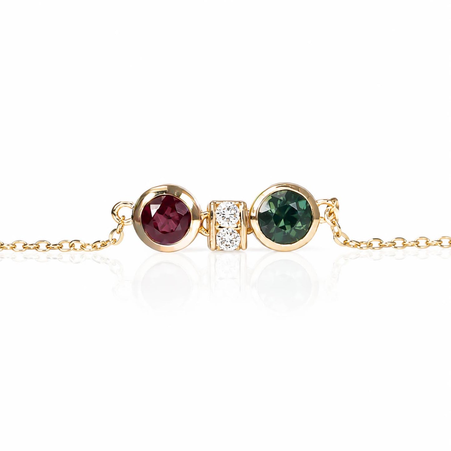 close-up of a bracelet featuring two round bezel-set gemstones, one natural ruby and one Australian teal sapphire, separated by accent diamonds shown on a white 