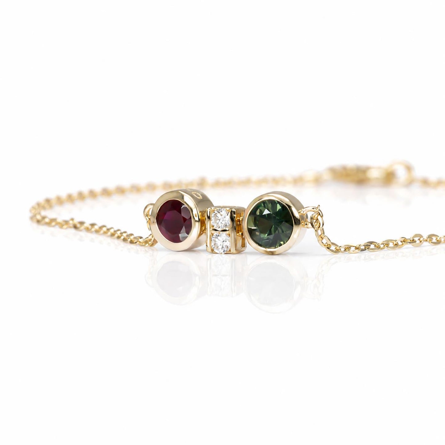 side view of a bracelet featuring two round bezel-set gemstones, one natural ruby and one Australian teal sapphire, separated by accent diamonds shown on a white 