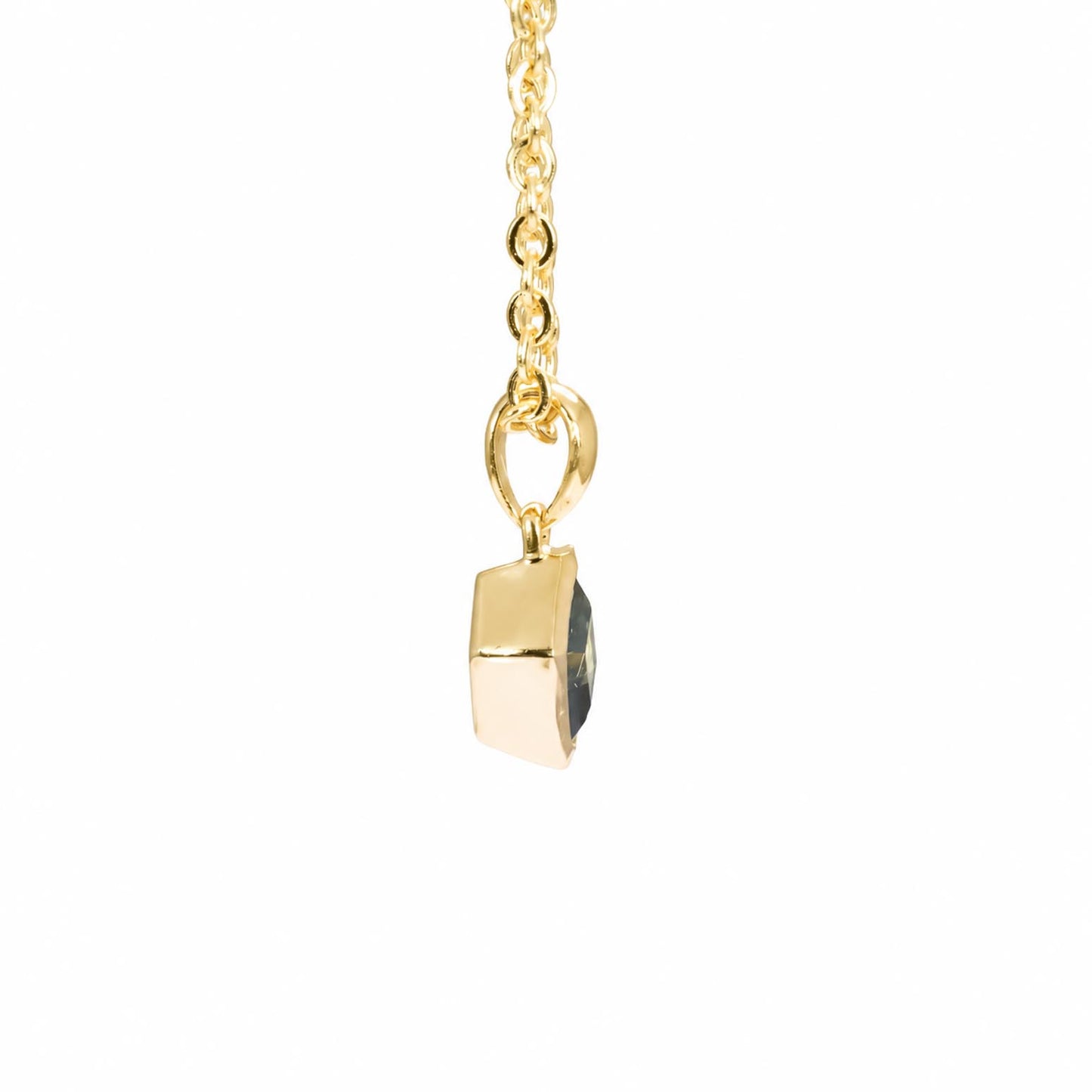 A gold pendant necklace featuring a small, faceted freeform teal sapphire, suspended from a delicate gold chain against a solid white background.
