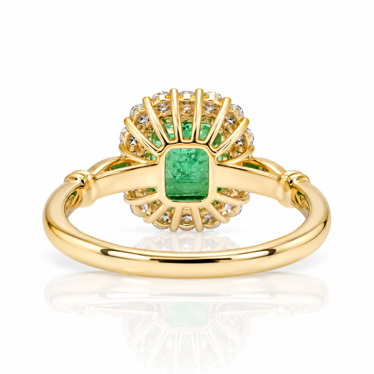 Back view of the setting of an emerald and diamond halo ring, shown on a white background with a soft reflection.