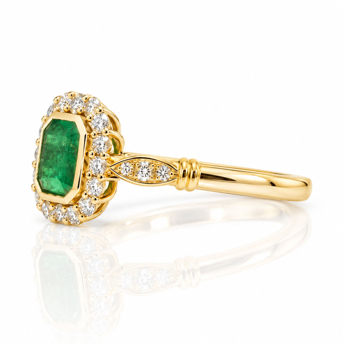 A yellow gold ring featuring a large emerald-cut Colombian emerald surrounded by a halo of diamonds, set on a polished gold band with a soft reflection on a white surface.