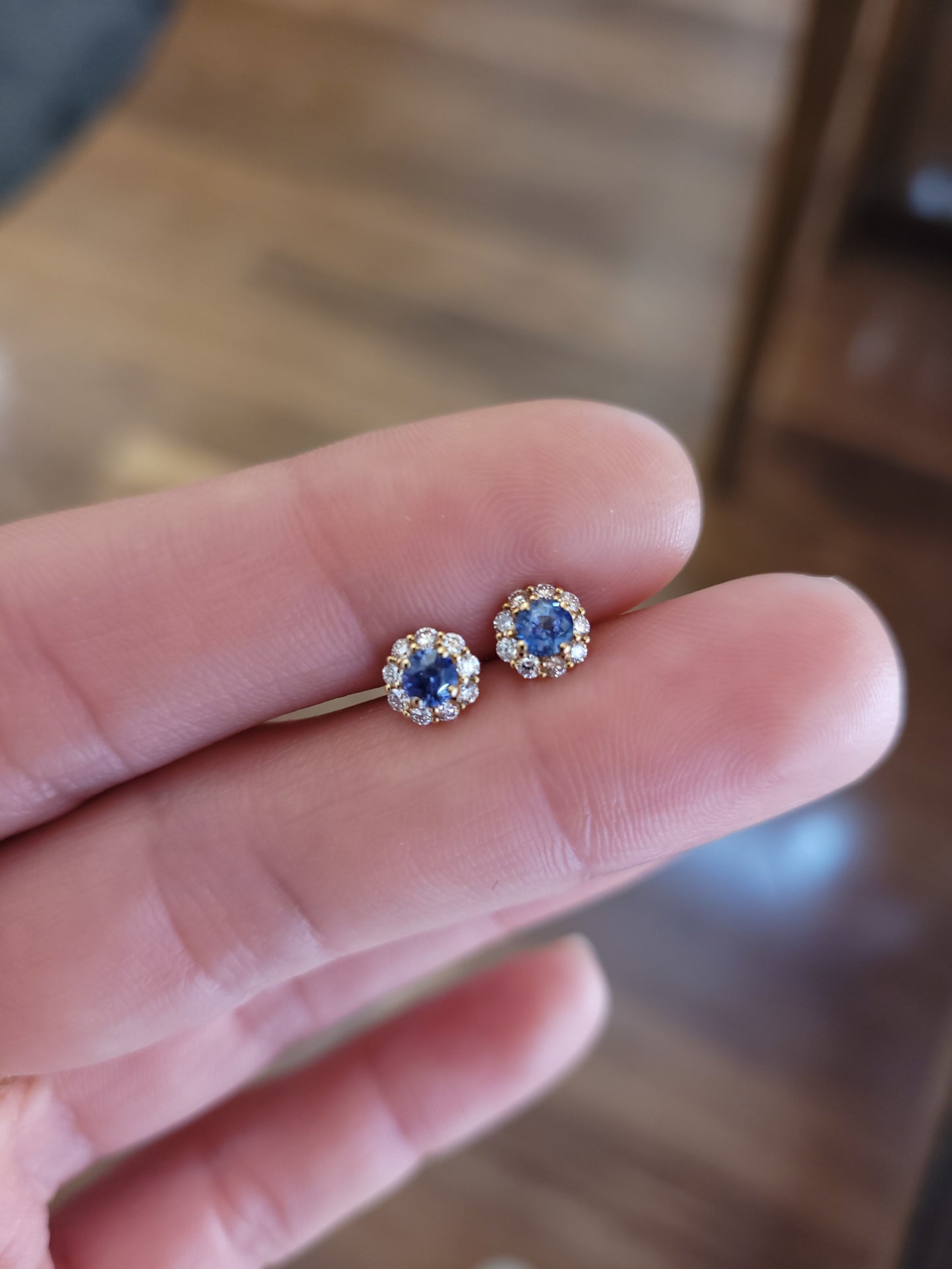 Blue gemstone earrings held between fingers with a blurred background
