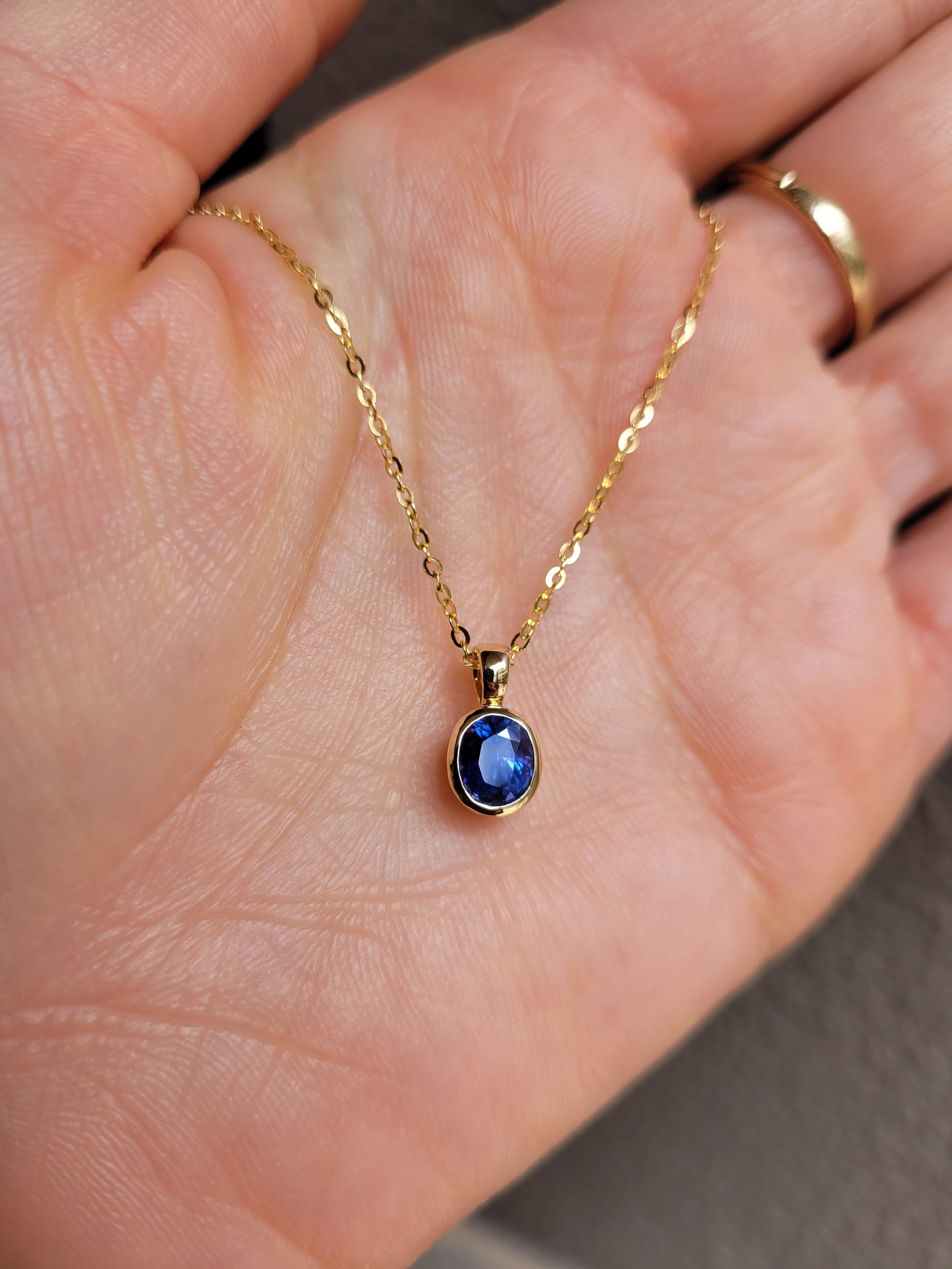 Gold necklace with a blue gemstone pendant held in a hand.