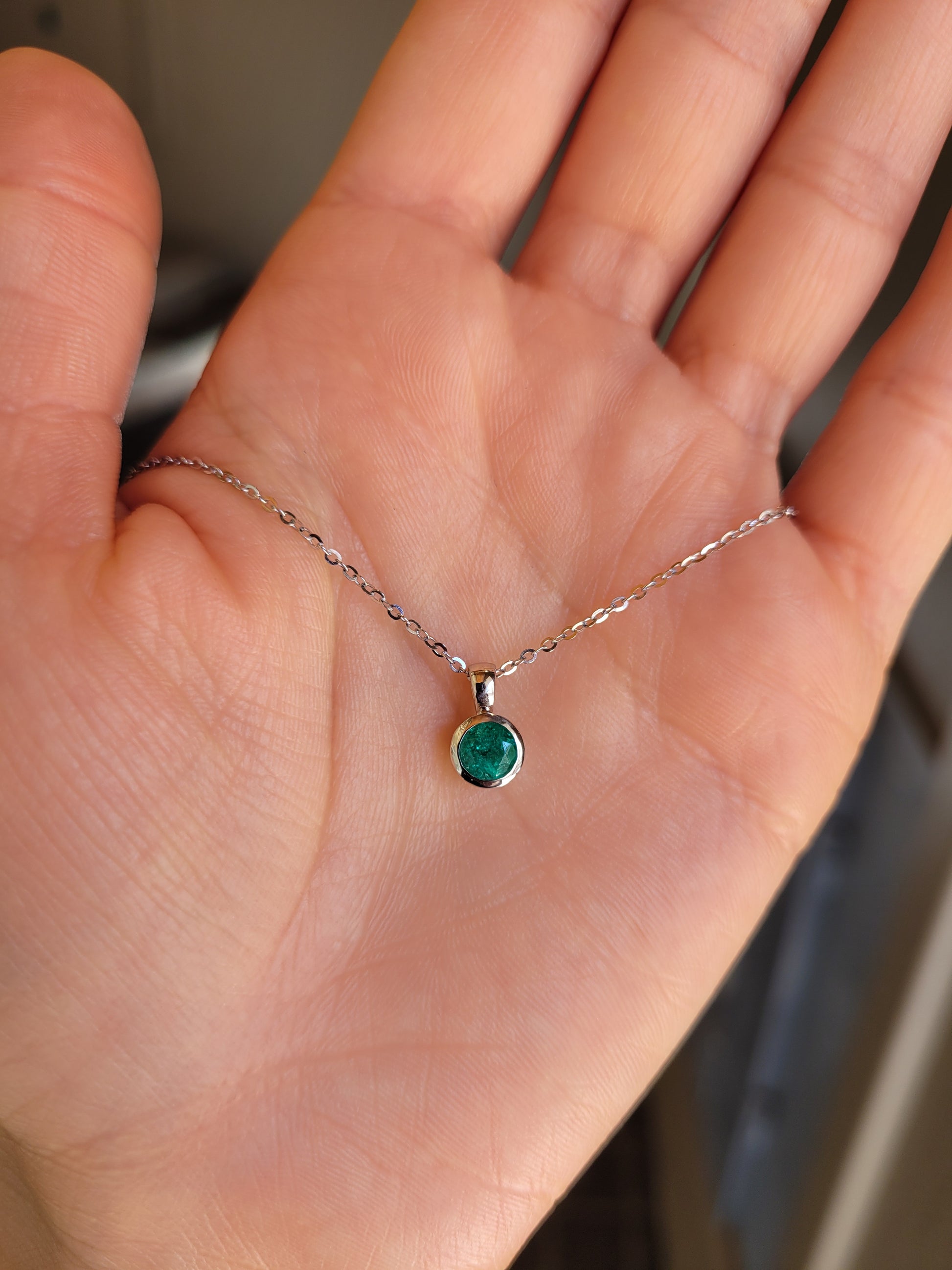Hand holding a delicate necklace with a green gemstone pendant.