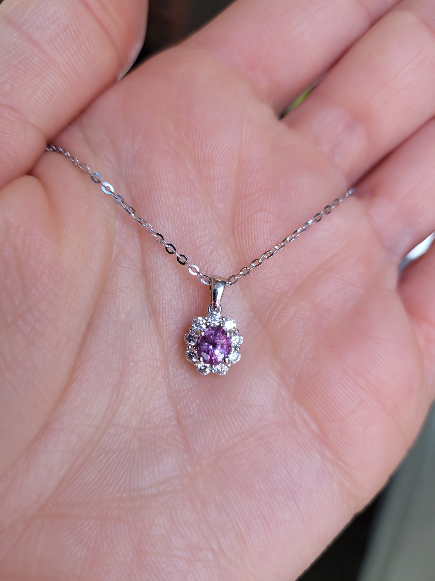 platinum necklace with a pink sapphire pendant held in a hand.