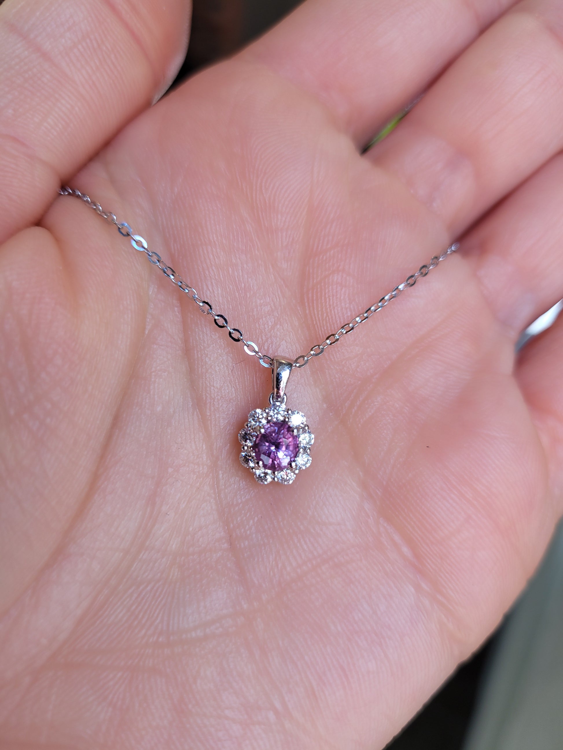 platinum necklace with a pink sapphire pendant held in a hand.