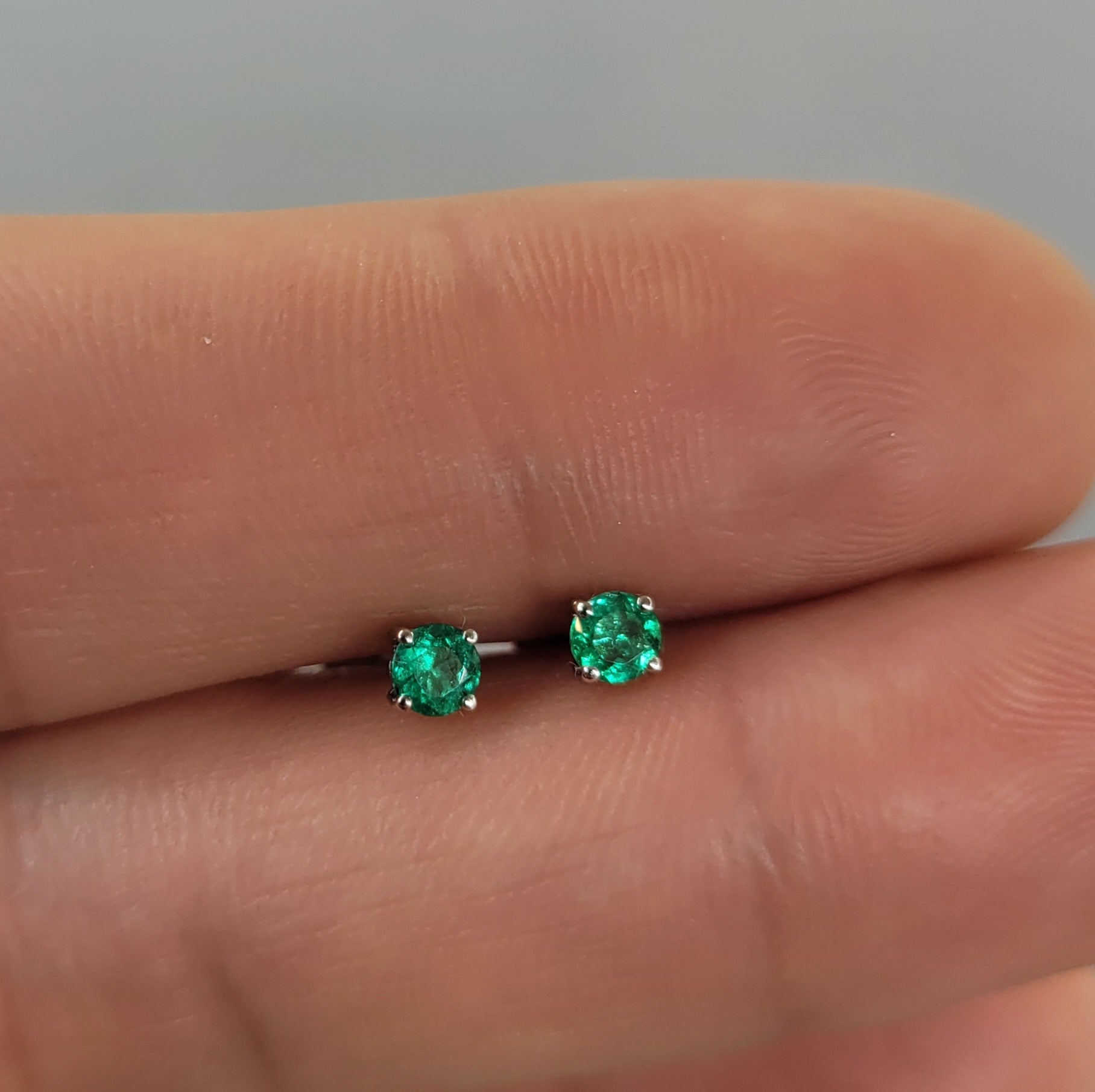 Pair of platinum stud earrings with emerald gemstones held on hand