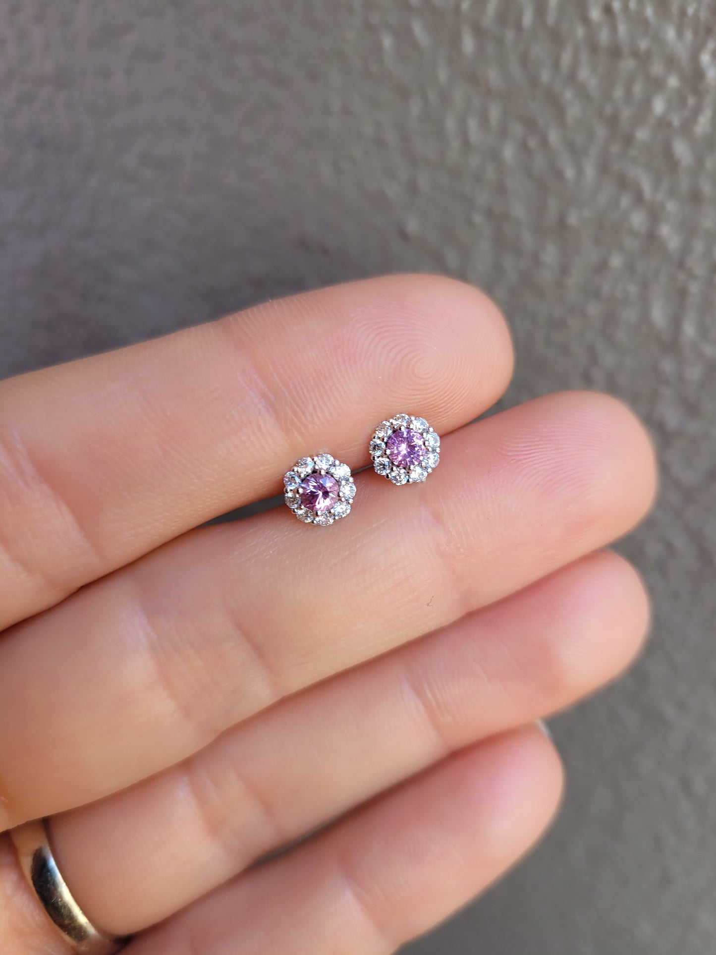Pair of pink sapphire earrings held between fingers against a neutral background