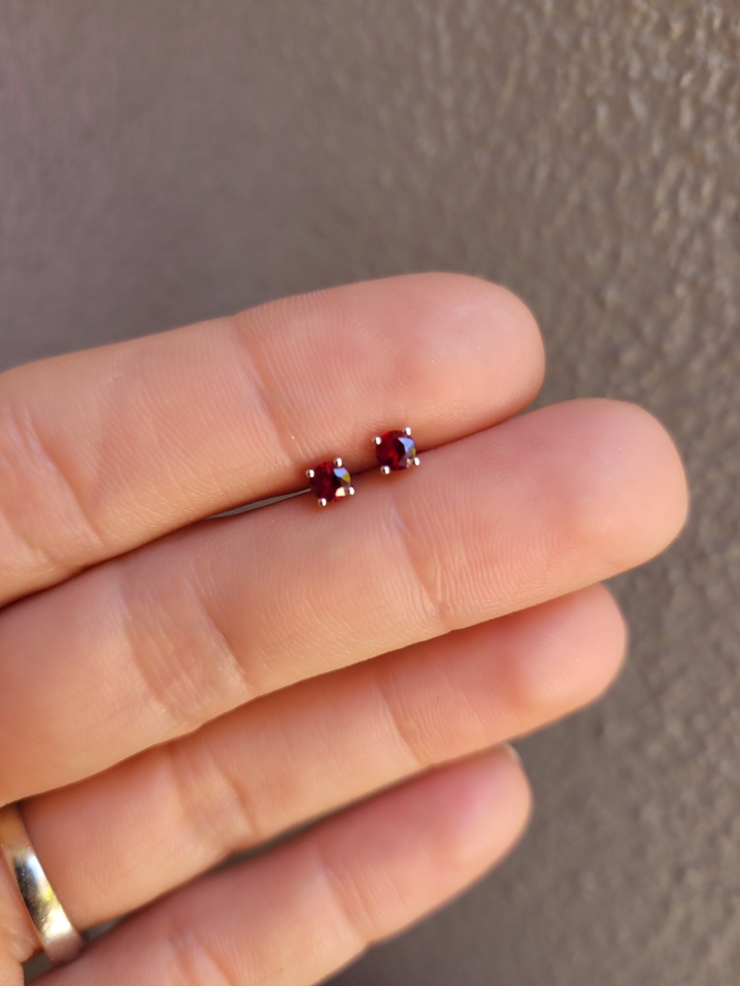 Ruby earrings in platinum held between fingers against a neutral background