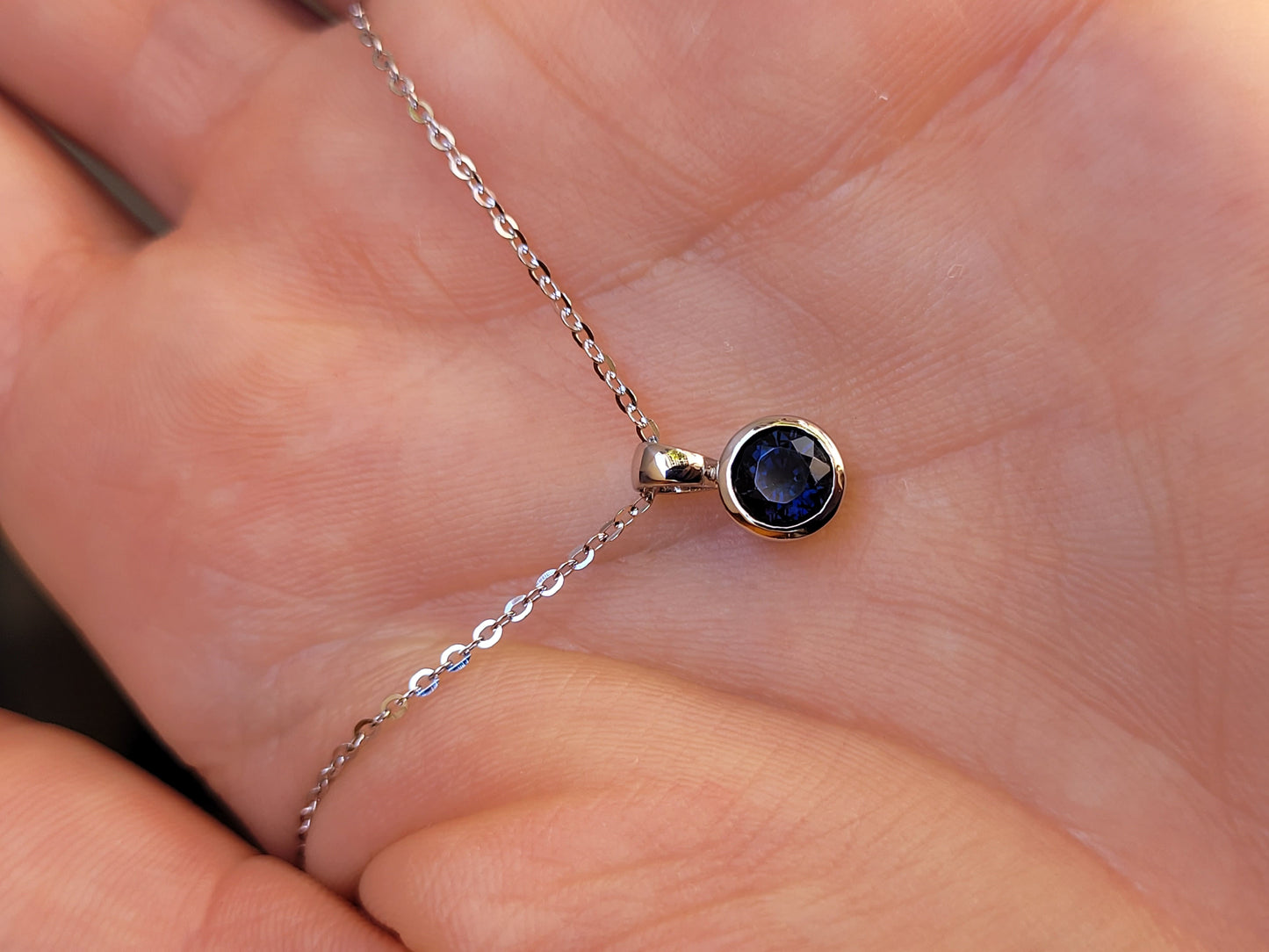 view on hand of platinum pendant with a blue sapphire on a gray background