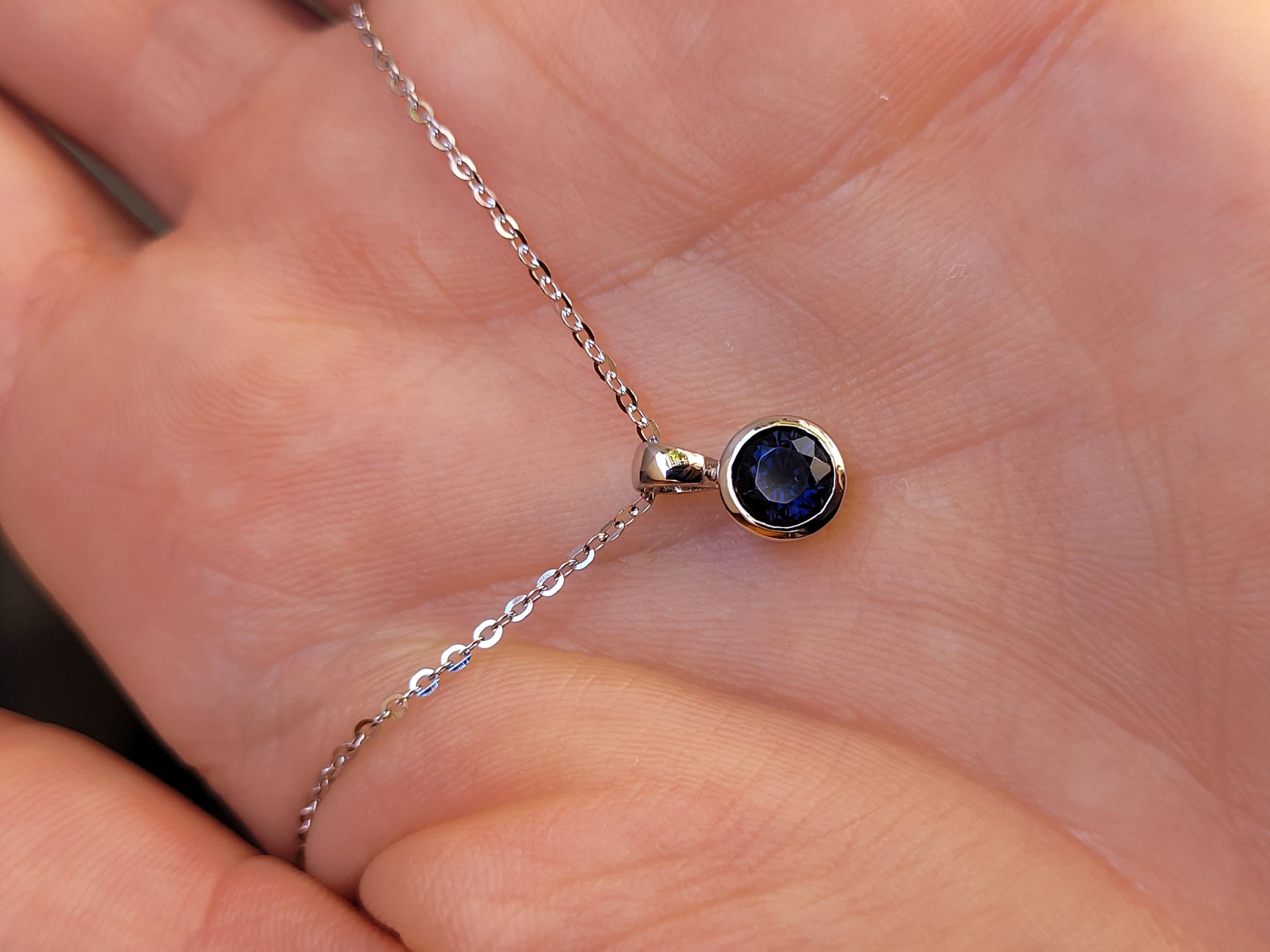 view on hand of platinum pendant with a blue sapphire on a gray background