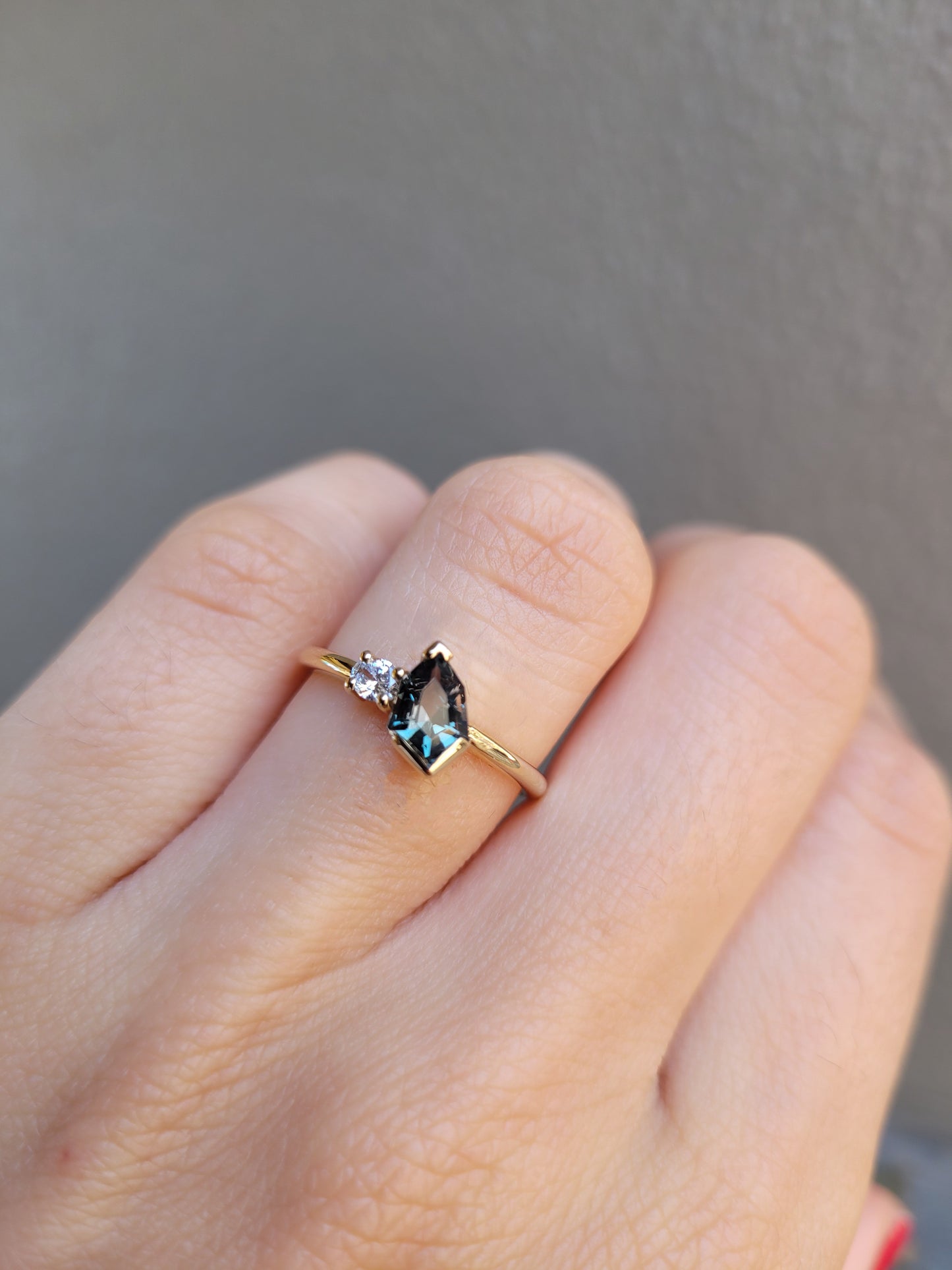 view on finger of toi et moi teal sapphire gold ring in gray background