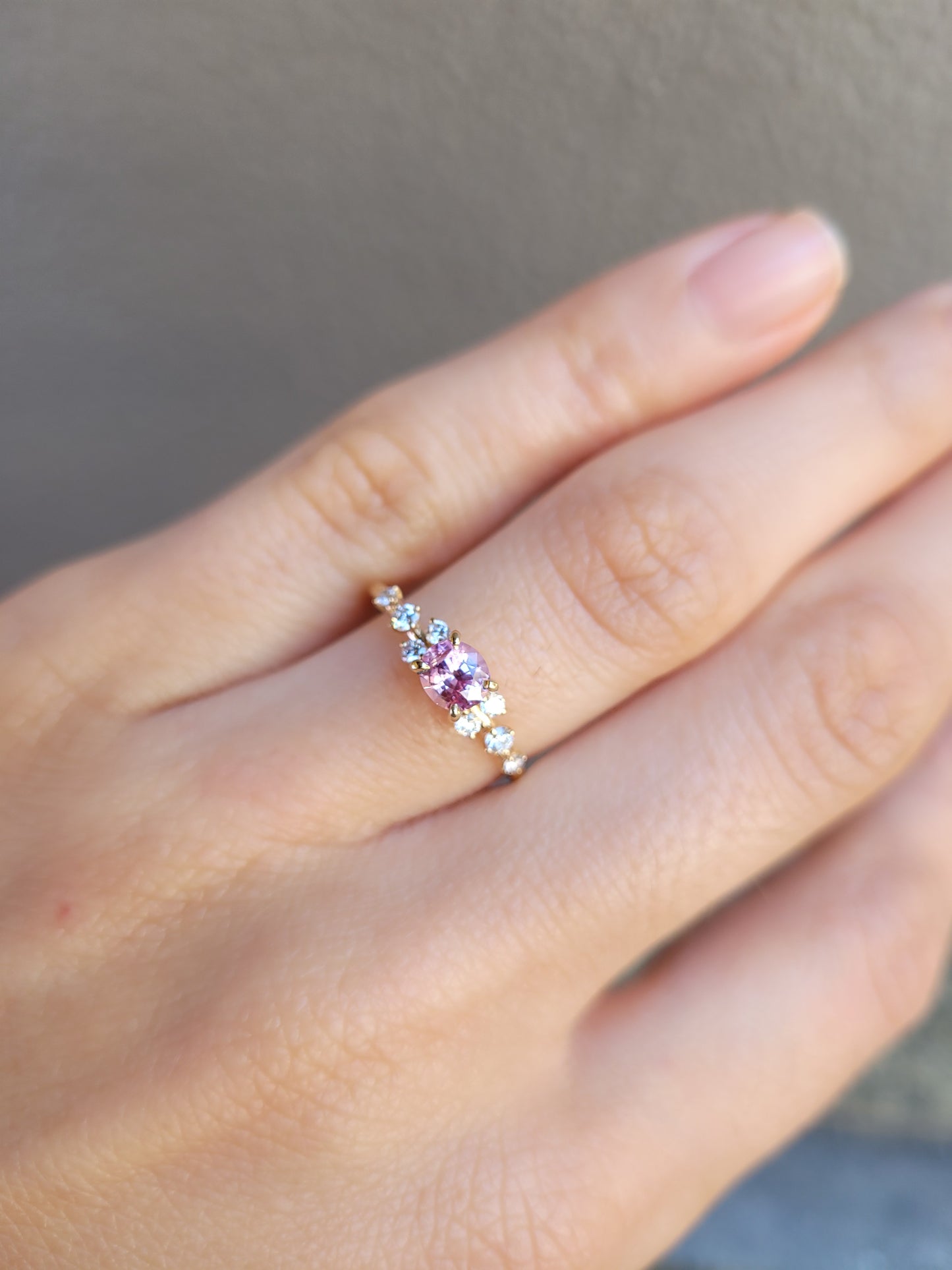 view on hand of Gold ring with natural pink sapphire and diamonds on a gray background
