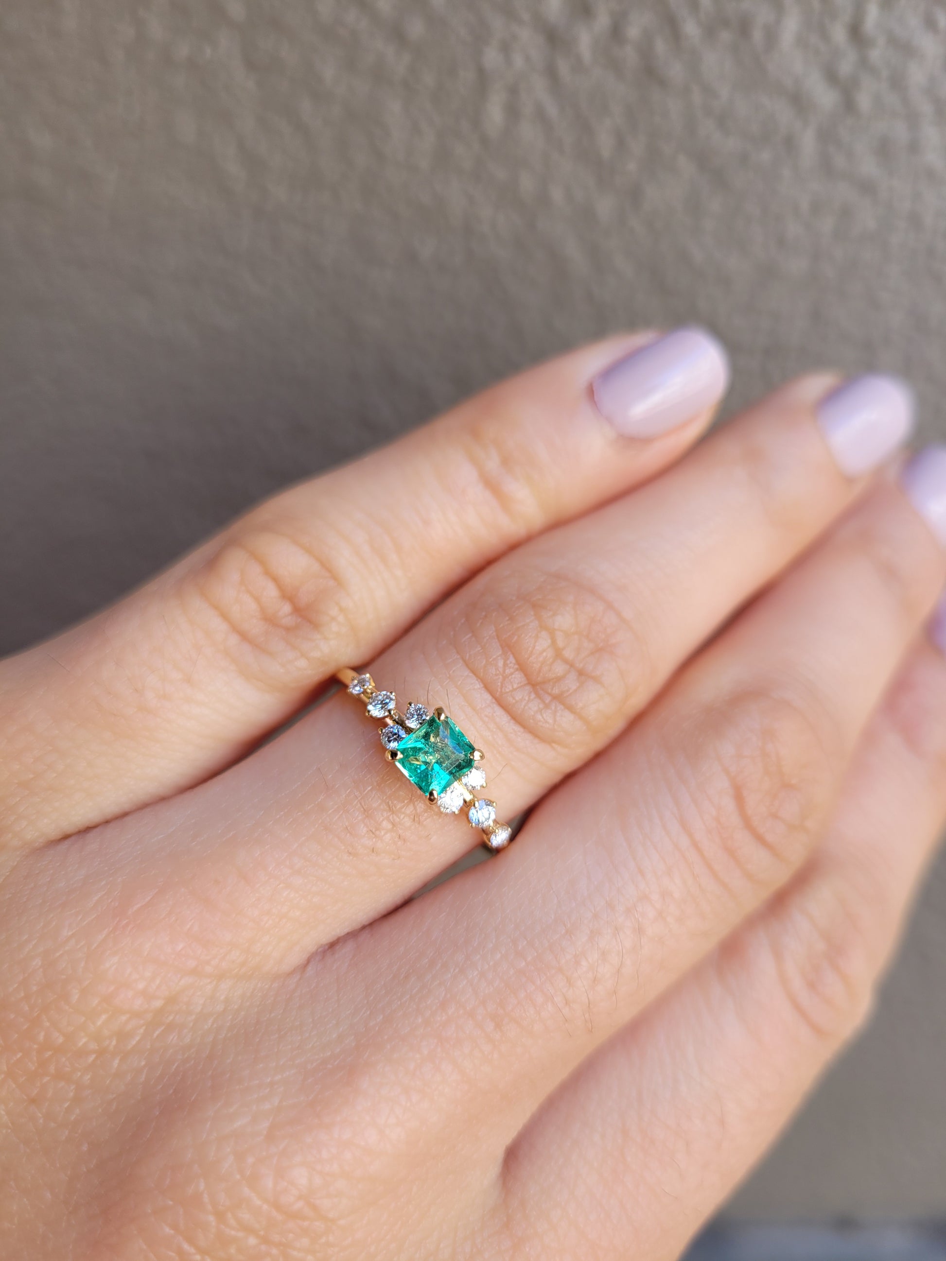 photo on hand of Yellow gold ring with Colombian emerald and diamonds on gray background