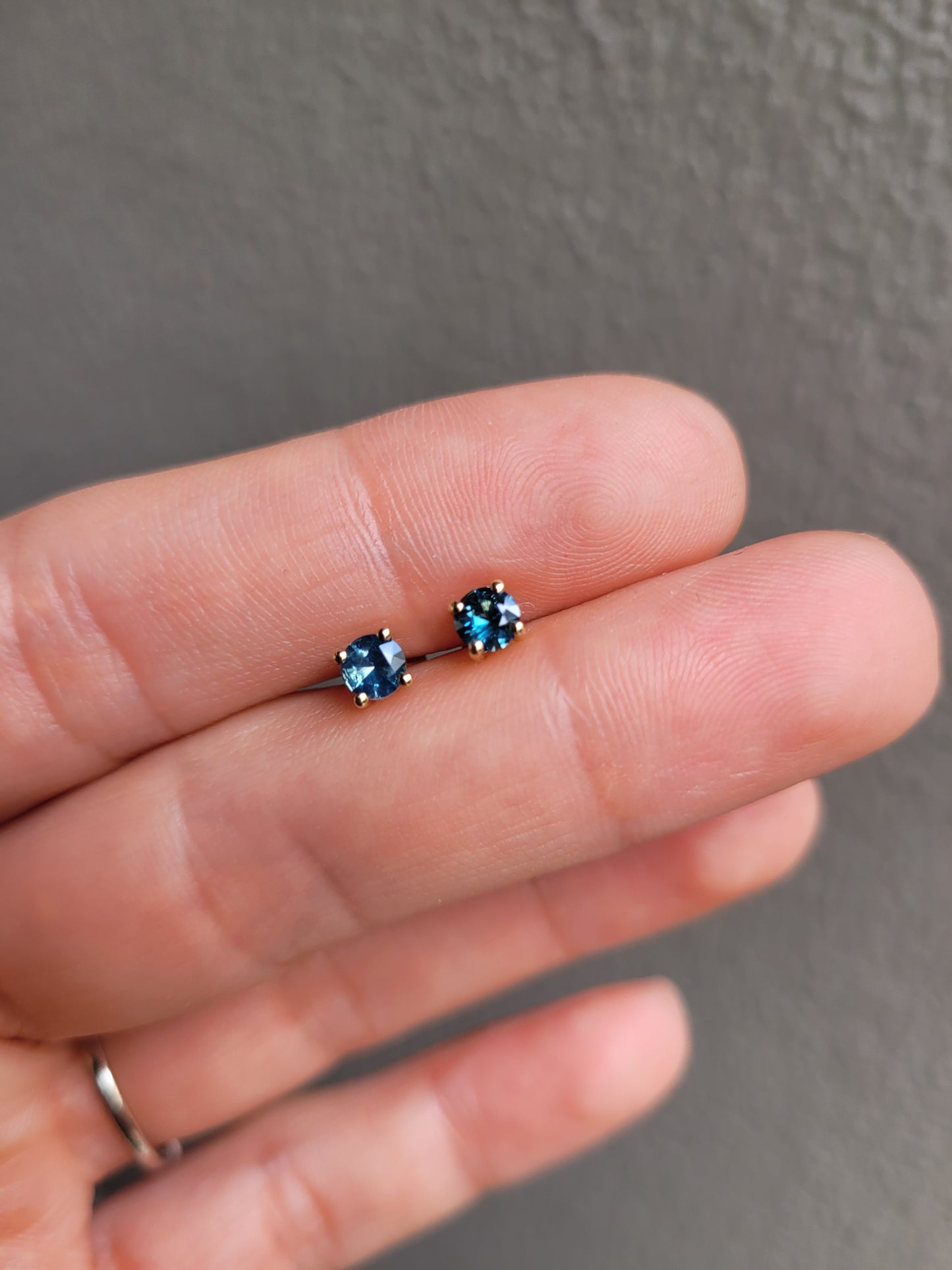 photo on hand of Australian teal blue sapphire gold stud earrings in gray background