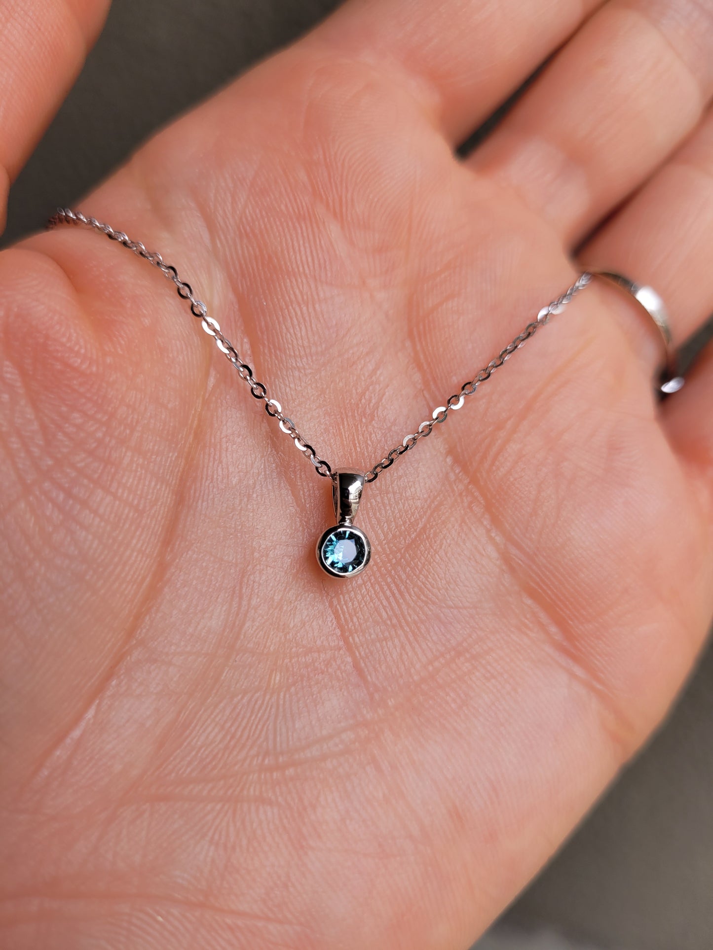 photo on hand of Australian teal sapphire platinum pendant in gray background