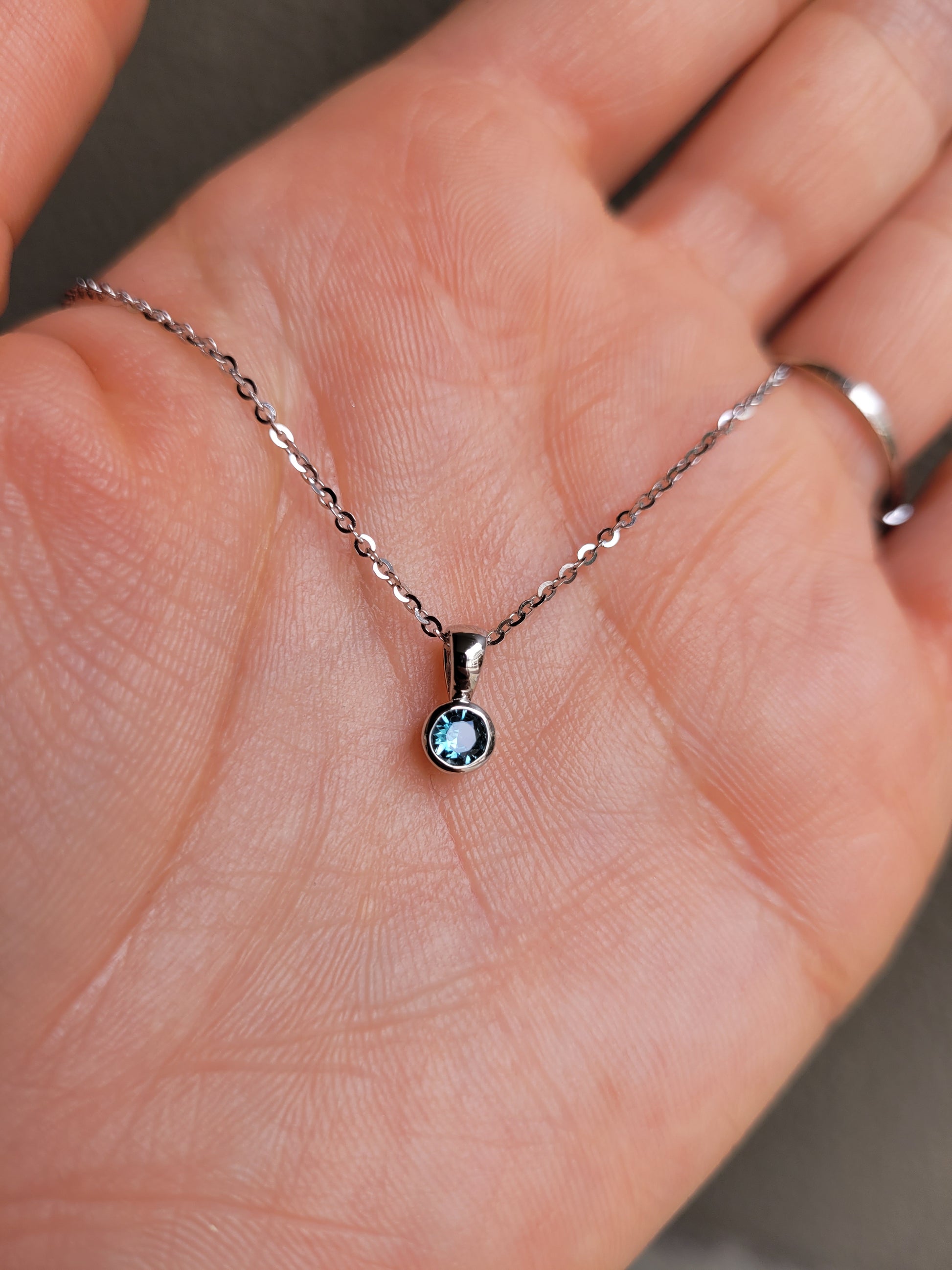 photo on hand of Australian teal sapphire platinum pendant in gray background